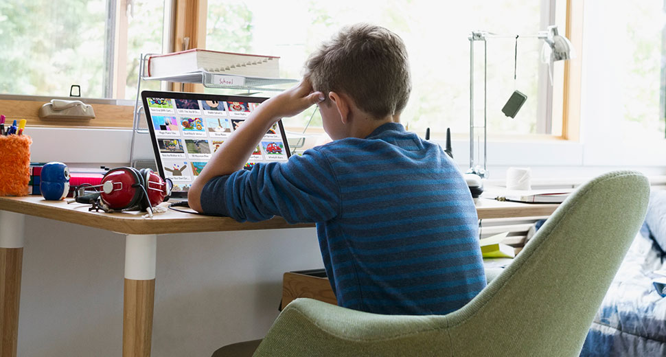 Boy sits at his desk whilst working on a laptop