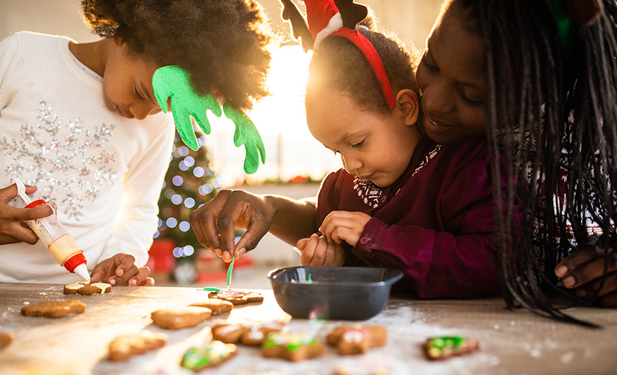 Two young girls learning how to ice christmas biscuits ready to give as presents