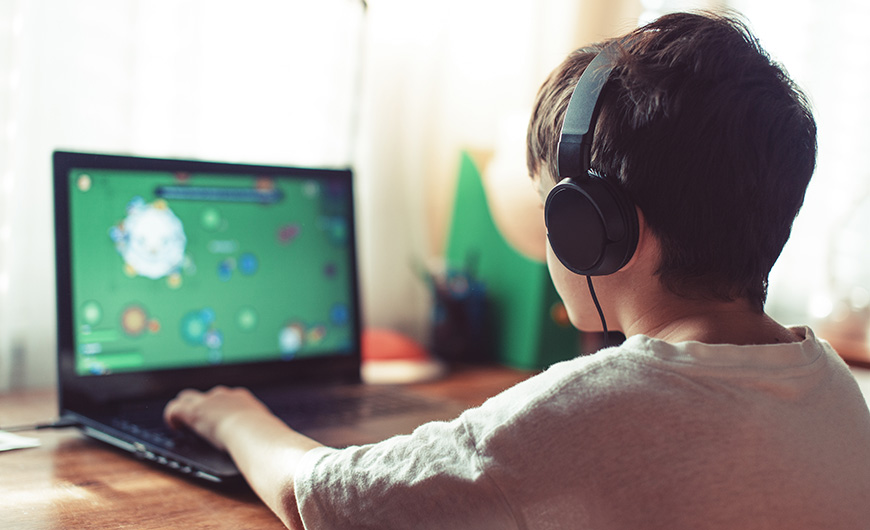 A boy plays a game on his computer whilst wearing headphones