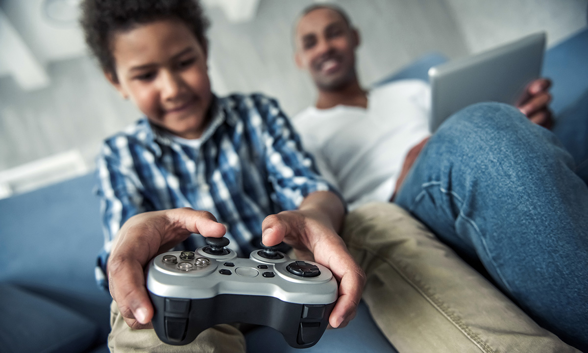 Young boy plays computer games, whilst his dad oversees