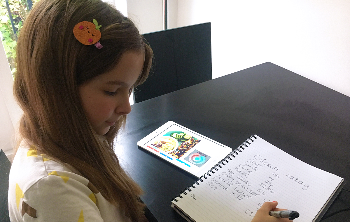 A young girl counts writes up a shopping list for a new recipe