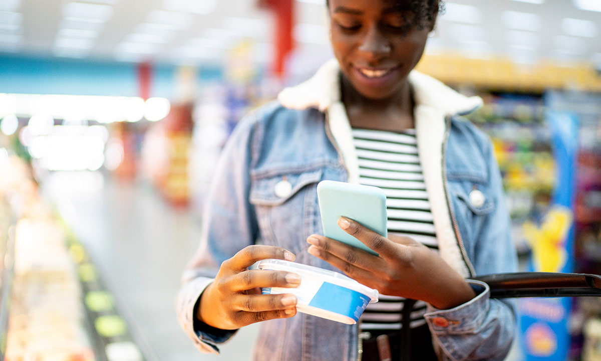 A girl holding up an item in a supermarket and scanning the barcode on her phone
