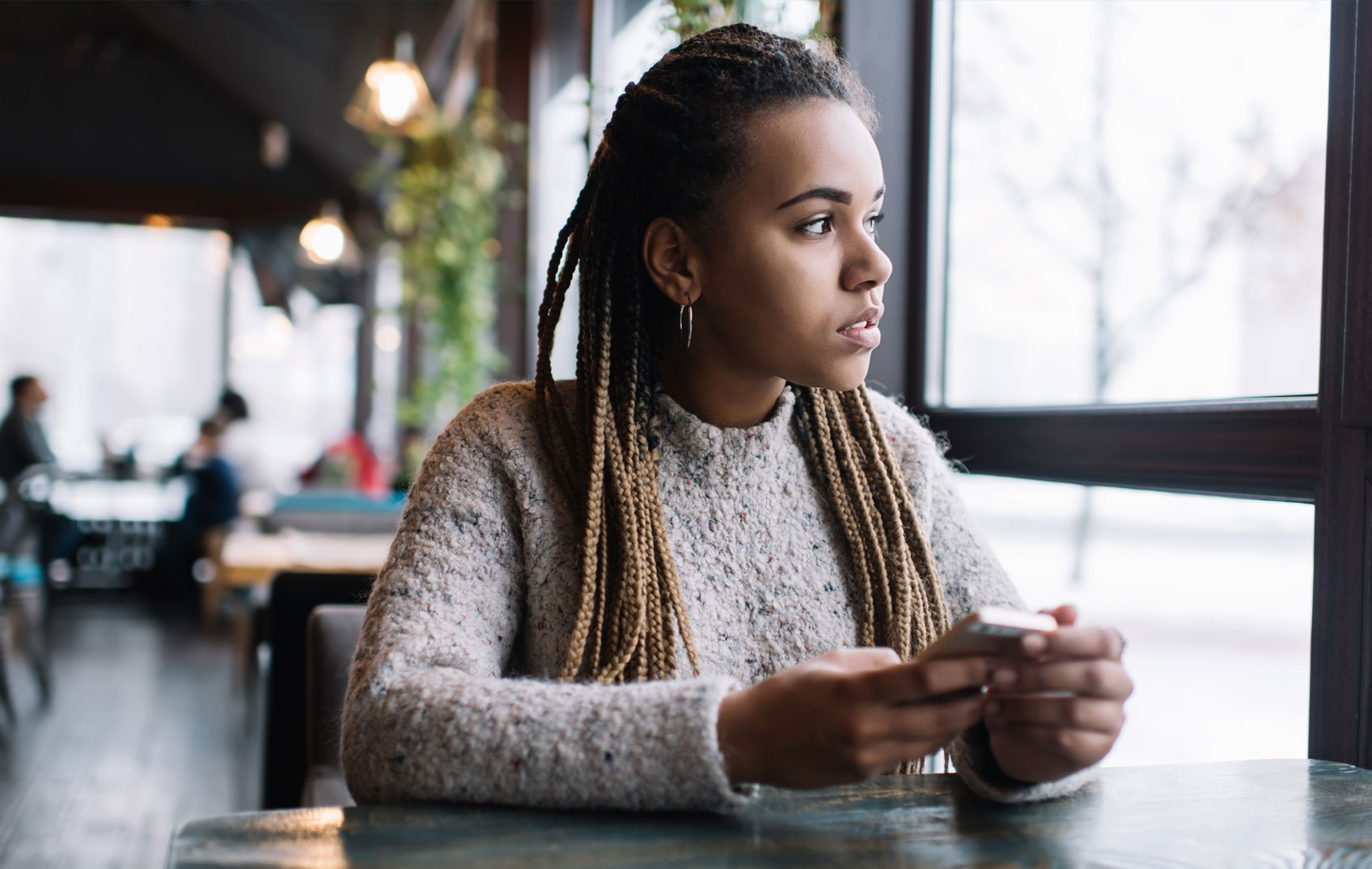 A young girl sits at a table in a cafe staring out of the window whilst holding her mobile