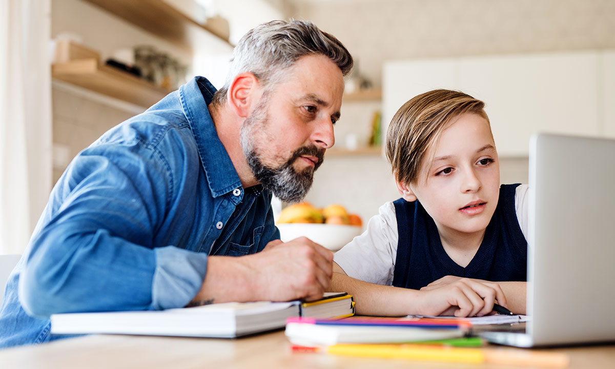 A father and son sit at their dining table working together on a laptop