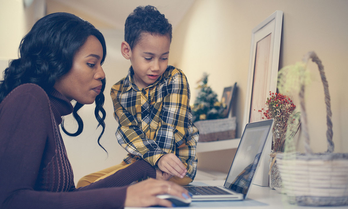 A mother and her son sit together at a laptop